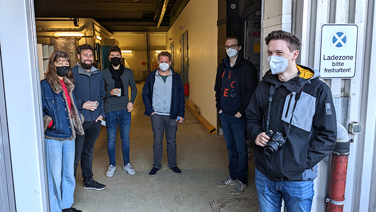 Prof. Dr. Oliver Gerberding (third from right) and his team follow the delivery of the vacuum chamber. In the future, they will be able to test the developed components for gravitational wave detectors under realistic conditions in the vacuum chamber